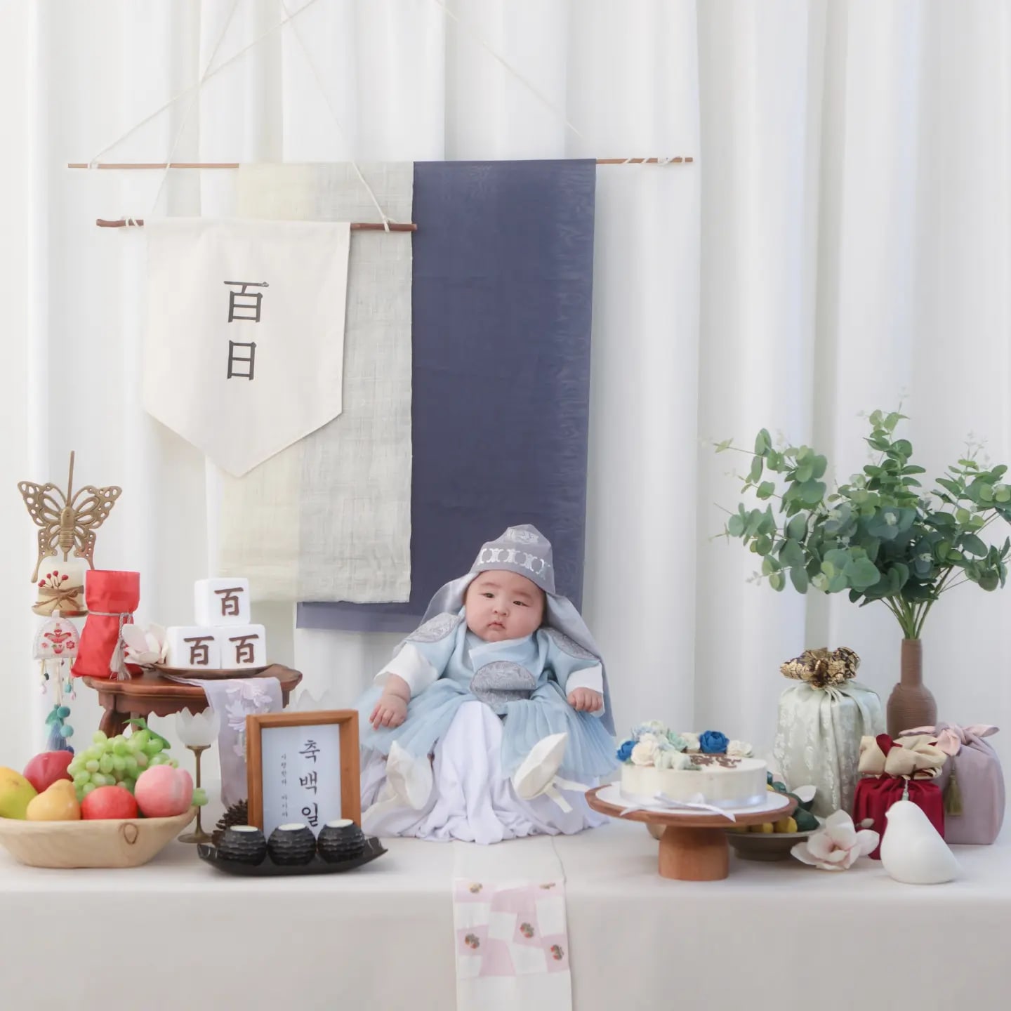 하늘색 한복을 입고 백일상에 앉은 아기