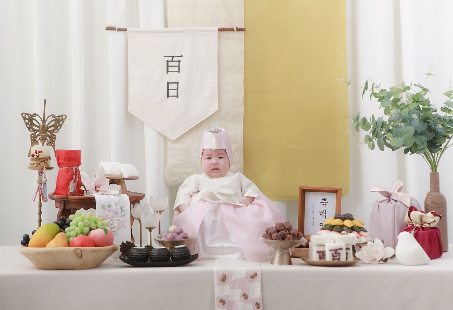 분홍 한복을 입고 백일상 중앙에 앉은 아기