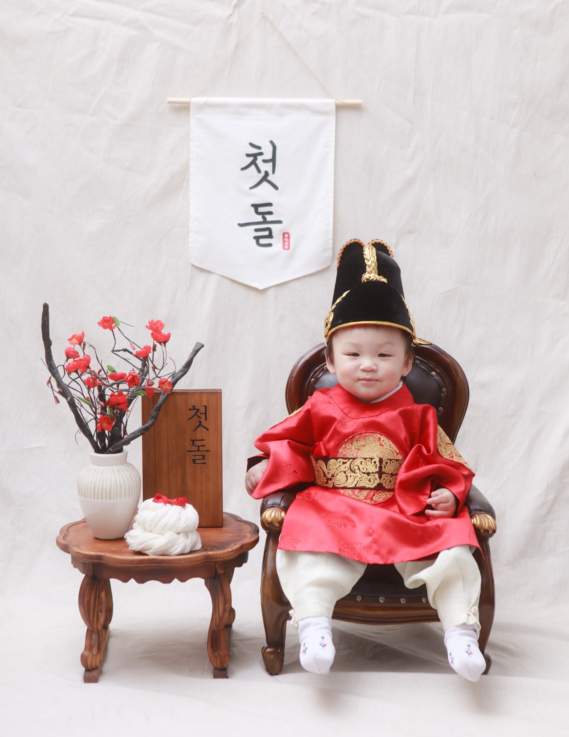 붉은 한복을 입고 첫돌 족자 앞에 앉은 아기